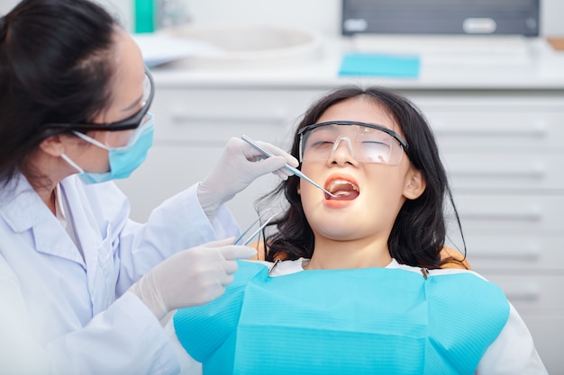 Paziente di sesso femminile seduta sulla poltrona del dentista con la bocca aperta durante la visita dal dentista per il controllo annuale