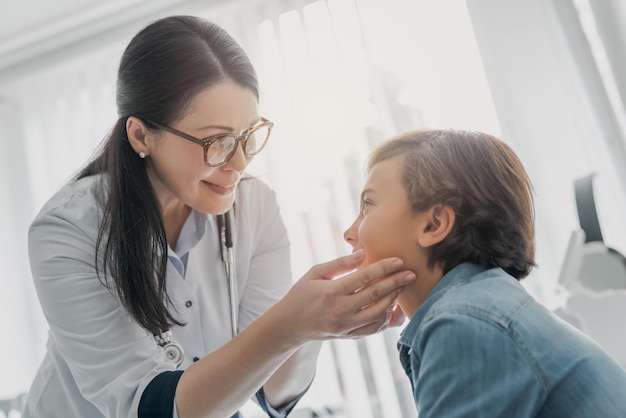 Female pediatrician examining gland of little boy in medical clinic