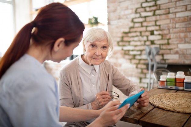 Female pensioner using tablet while sitting near caregiver