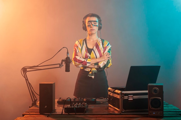 Photo female performer posing with arms crossed at turntables, using headphones and mixer to produce techno music or sounds. doing performance with mixer and control buttons, audio stereo equipment.