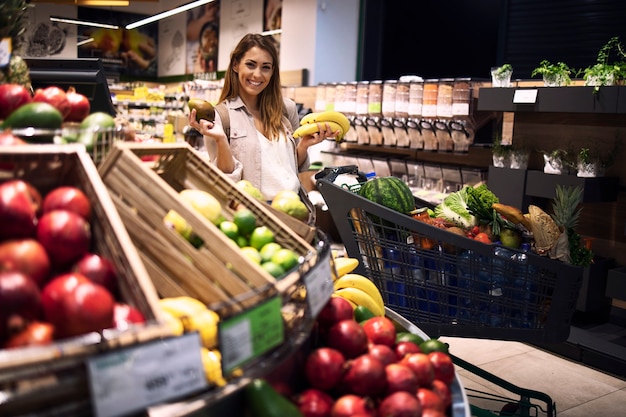 Female person holding fruits in supermarket and smiling.