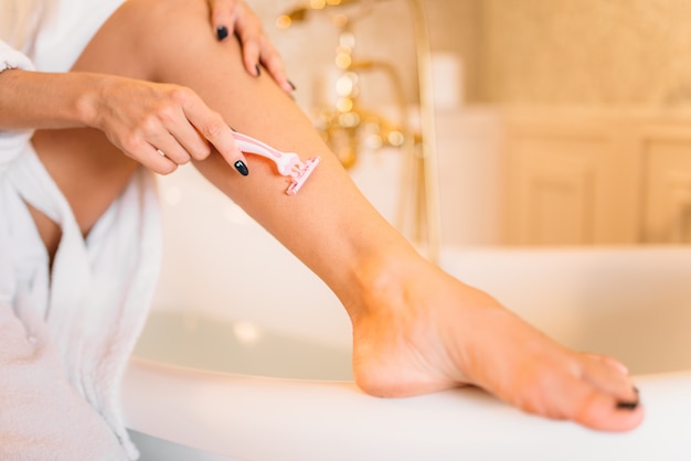 Female person shaves legs in bathroom