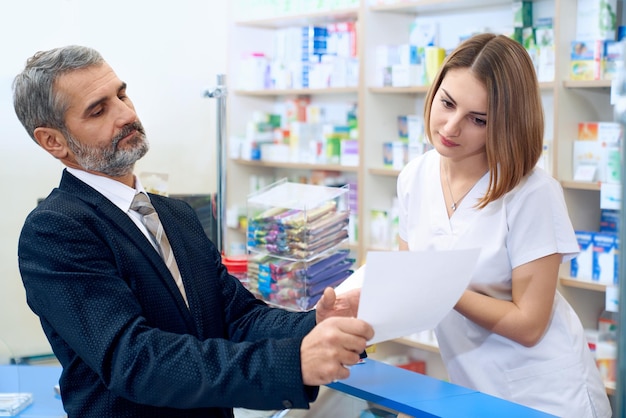 female pharmacist at counter reading prescription with customer