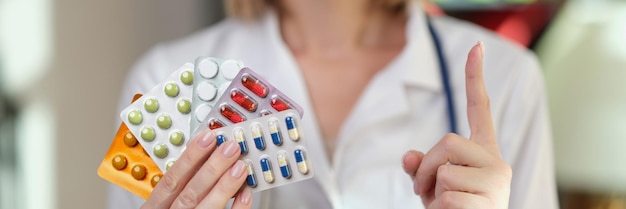 Female pharmacist holds packs of medical pills and points her finger up warning and reminder to