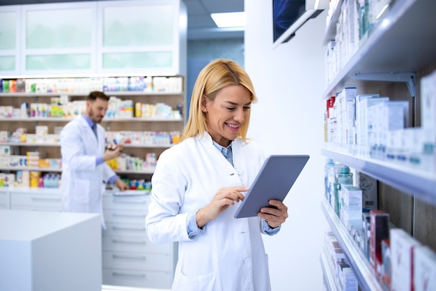 Female pharmacist in white coat checking medicine availability for online orders.