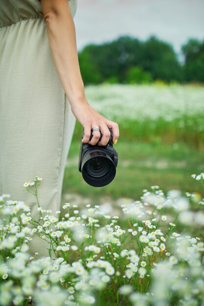 花畑の風景に屋外でカメラを持っている女性写真家、認識できない女性が彼女の手にデジタルカメラを持っています。旅行自然写真、テキストのためのスペース。