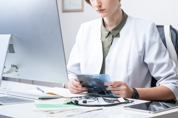 Foto medico femminile all'ufficio moderno del medico. donna che esamina i raggi x sul posto di lavoro davanti a un computer desktop