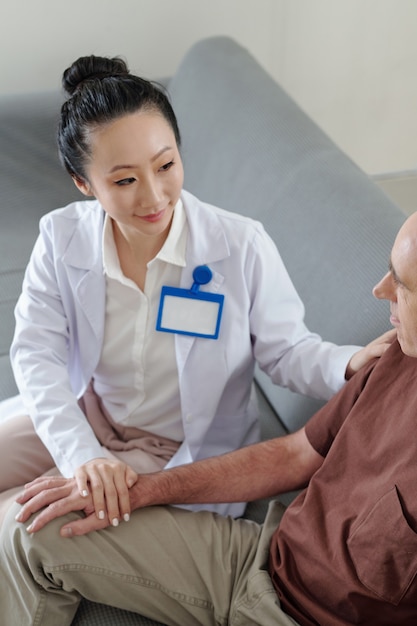 Female physician talking to mature patient when visiting him at home