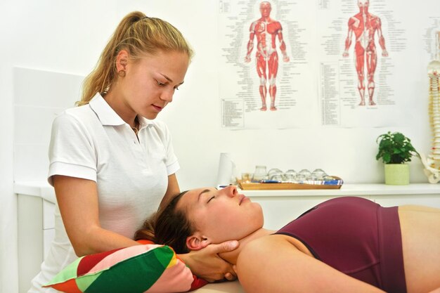 Female physiotherapist massaging muscles on neck of her client lying at table