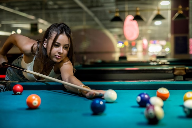 Female player playing pool and aiming the billiard ball with cue