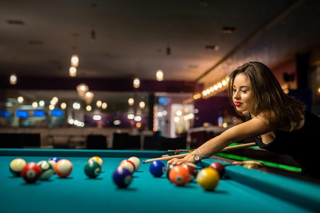 Female player playing pool and aiming the billiard ball with\
cue