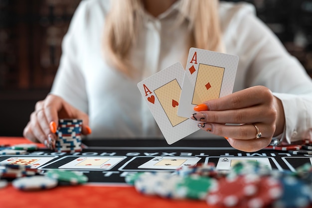 женщина-игрок показывает два туза и азартные фишки в игре в покер за столом казино