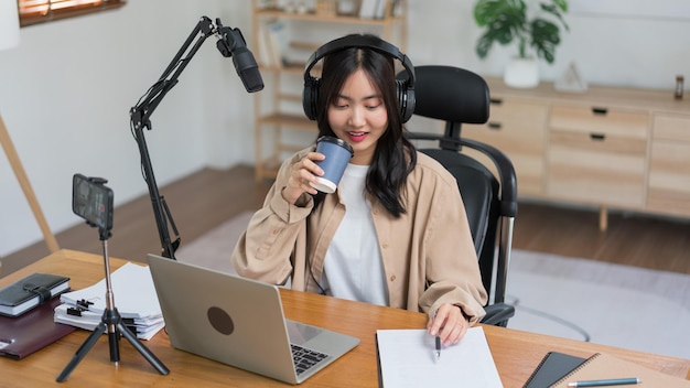 Female podcaster drinking coffee and writing note in paper while working to recording video podcast