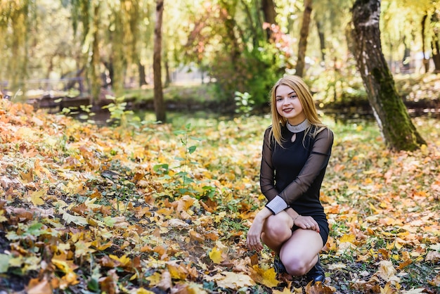 Female porteait in autumn park. Beaurtiful woman in black dress posing with yellow trees