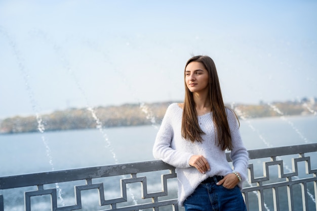 Female portrait. Beautiful woman in casual wear posing on lakeshore with fountain