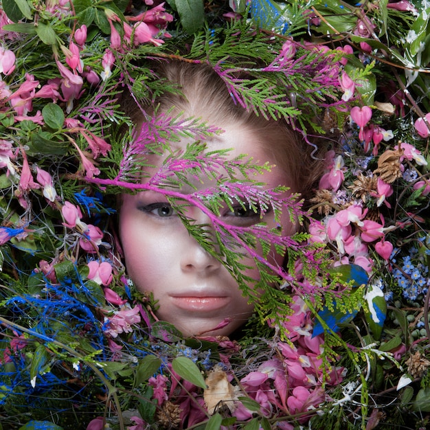 Photo female portrait in fairy tale stylisation surrounded with natural plants and flowers.