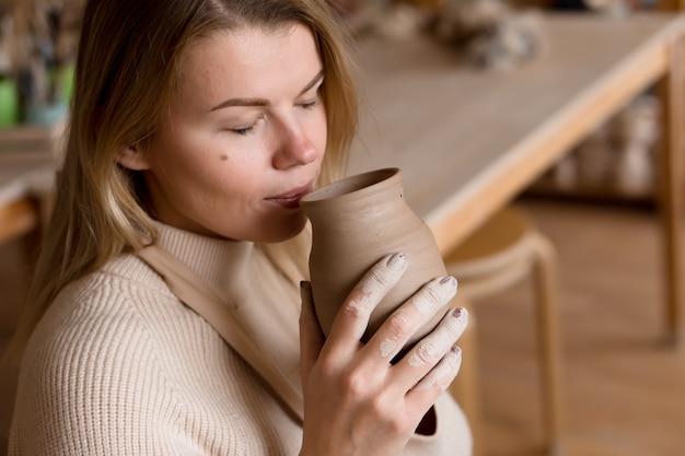 female potter is sniffing just made vase wet clay smells like a river