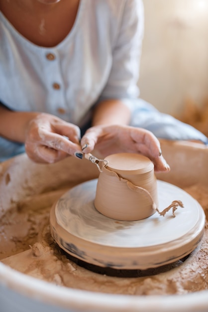 Female potter removes the extra layer on pot, pottery wheel.