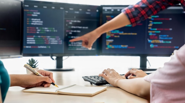現代のオフィス会社でコンピューターがプログラムコードを表示しながら、若い熟練したWeb開発者がプログラムを提示しながらメモを取る女性プログラマーJavaスクリプトWebデザインコンセプト急成長