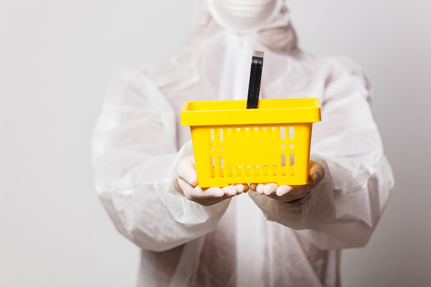 female in protection suit holds shopping basket