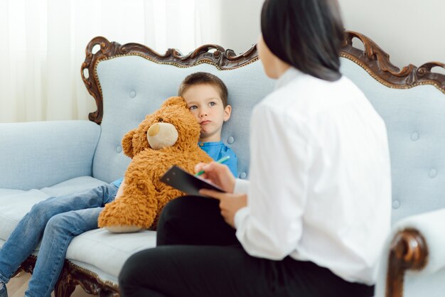 Female psychologist calming cute little boy in office