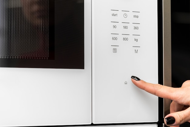 Female pushes button on microwave oven close up