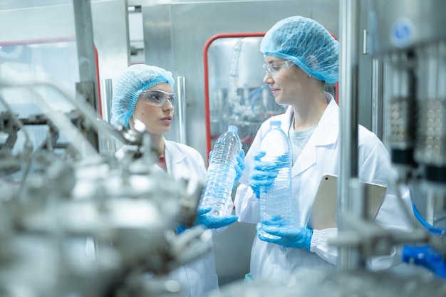 Female quality control worker inspecting water bottle on production line in drinking water factory