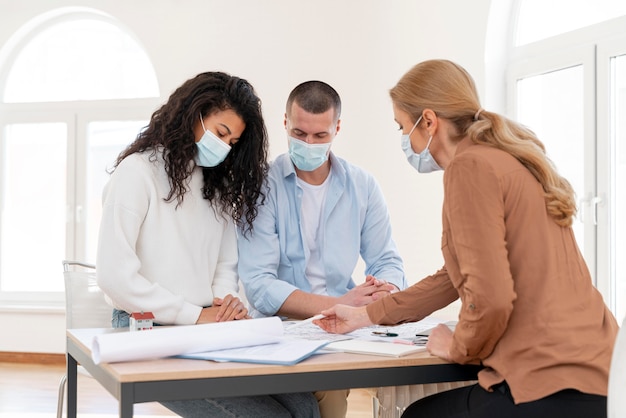 Foto agente immobiliare femminile con mascherina medica che mostra i piani di casa coppia