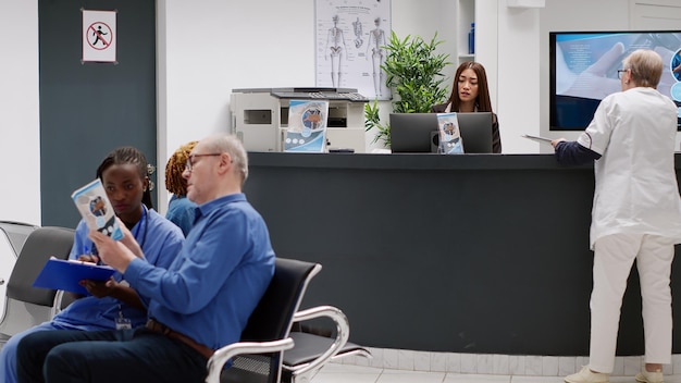 Female receptionist talking to senior doctor at reception\
counter in medical facility waiting area. general practitioner\
asking worker about medical reports and healthcare\
appointments.