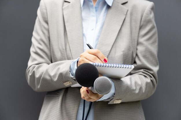 Foto reporter donna in una conferenza stampa o in un evento mediatico che scrive note tenendo un microfono