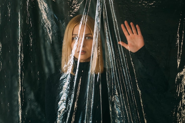 Female rights Defocused art portrait Freedom independence Anxious blonde woman trapped behind wrinkled transparent polyethylene film isolated on black background out of focus