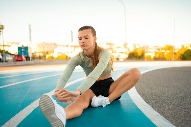 Female runner doing stretching exercises sitting on running track