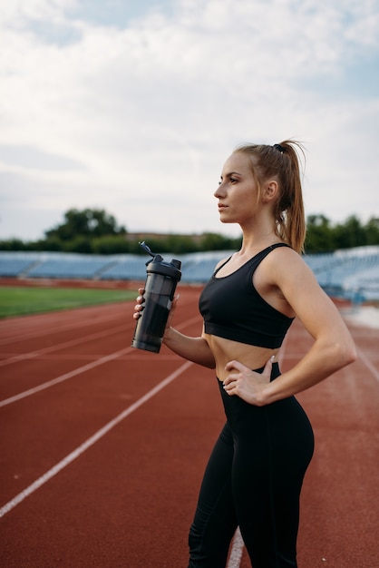 Female runner drinks water, training on stadium