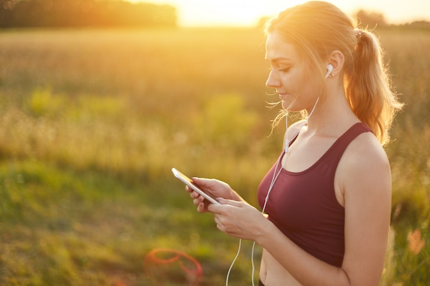 Female runner enjoying calm atmosphere while jogging on field, listening to her favourite track in earphones