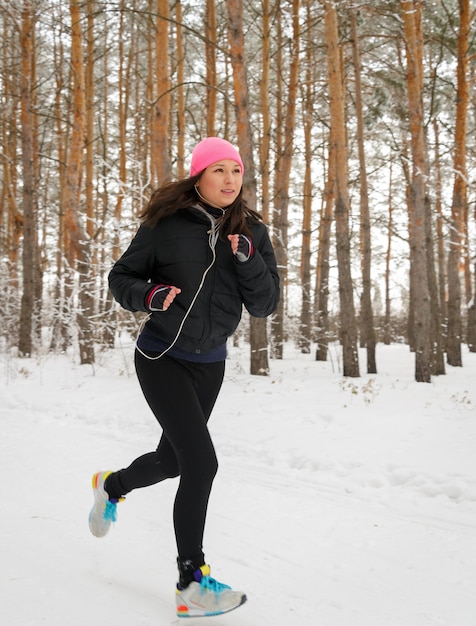 Фото Женщина-бегун на бегу в холодном зимнем лесу в теплой спортивной беговой одежде и перчатках с наушниками.