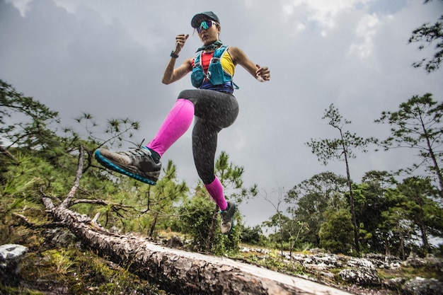 Foto il corridore femminile salta sopra un albero di pino durante un trail run sotto la pioggia