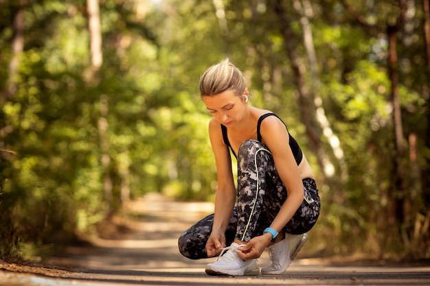 Female runner lacing her sneakers on a forest trail.