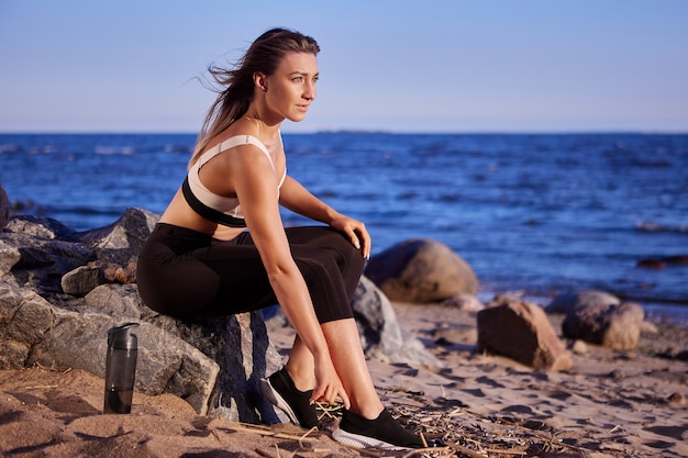 Female runner sits near seaside during running for rest