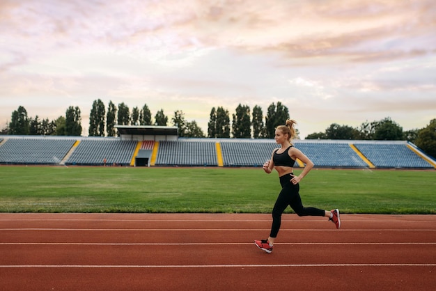 Foto corridore femminile in abbigliamento sportivo allenamento di jogging sullo stadio donna che fa esercizio di allungamento prima di correre in arena all'aperto