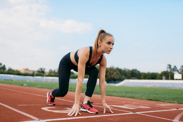 スタートラインでのスポーツウェアの女性ランナー、スタジアムでのトレーニング。屋外アリーナで実行する前にストレッチ運動をしている女性