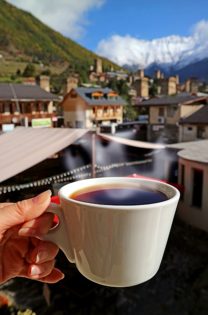 Mano femminile che tiene una tazza di caffè caldo con vapore contro la vista sfocata del paese country