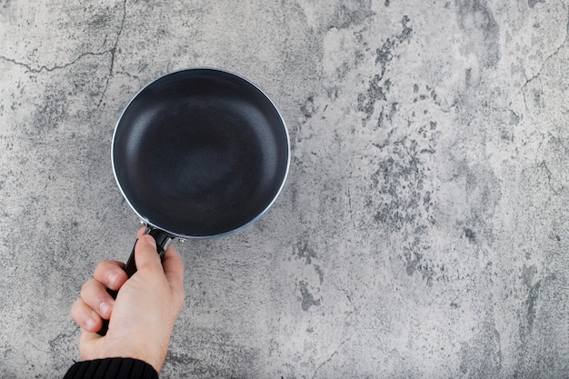 Female's hand holds frying pan on a stone background . 