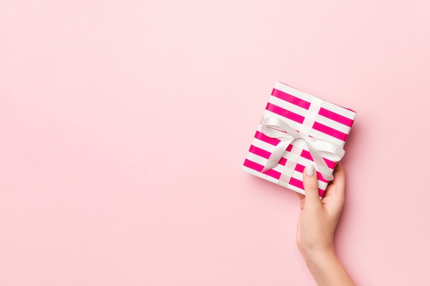 Female's hands holding striped gift box with colored ribbon on living coral. 