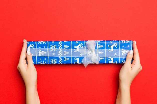 Photo female's hands holding striped gift box with colored ribbon on red.