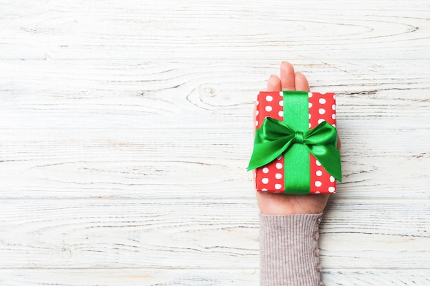 Le mani della femmina che tengono il contenitore di regalo a strisce con il nastro colorato su legno rustico bianco