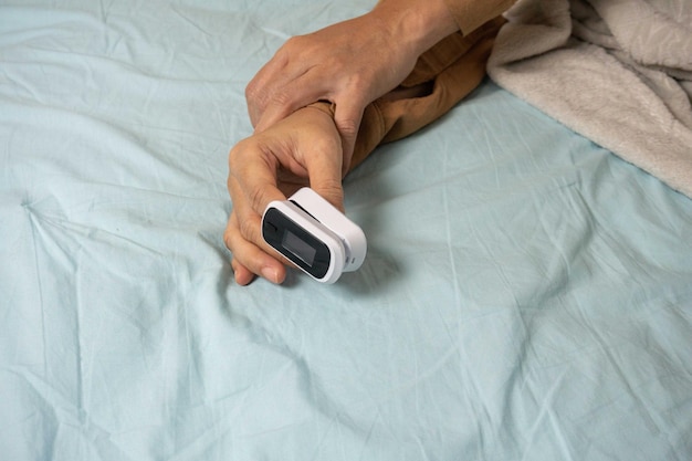 Photo female's hands with a pulse oximeter at the index finger woman lying at the bed gadgets for health