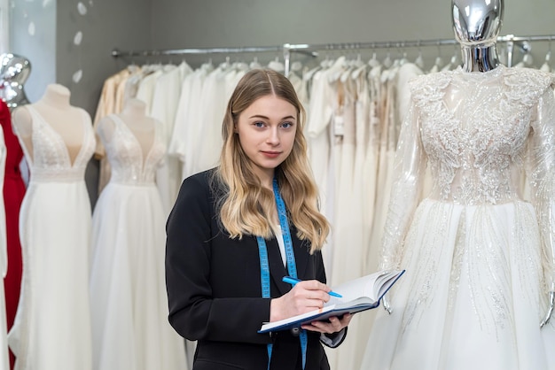 Female saleswoman holding a notebook and posing in a salon selling wedding dresses