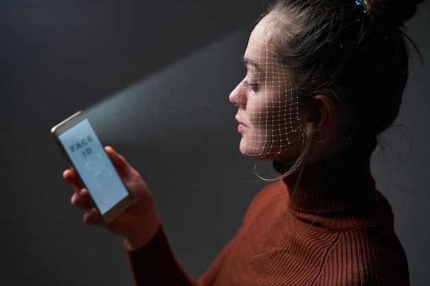 여성은 생체 인식을 위해 휴대 전화의 안면 인식 시스템을 사용하여 얼굴을 스캔합니다. 미래의 첨단 기술과 얼굴 ID