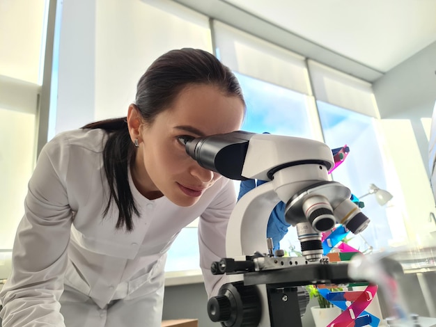 Foto chimico femminile dello scienziato che guarda tramite il microscopio nel concetto di test di paternità del dna del laboratorio