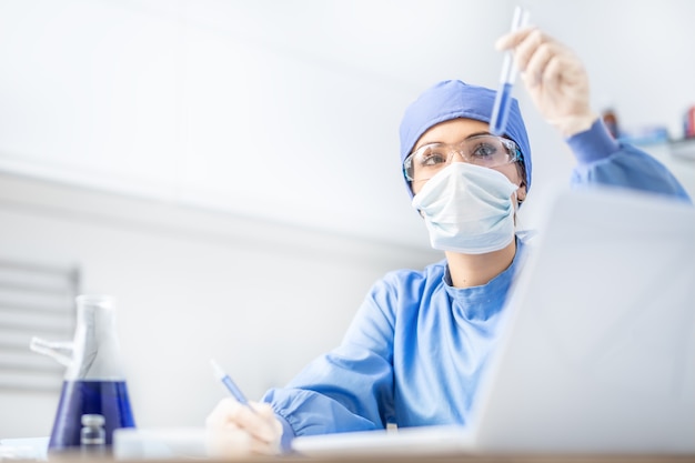 Female scientist or doctor specialist working in laboratory. Examines a substance in a test tube.